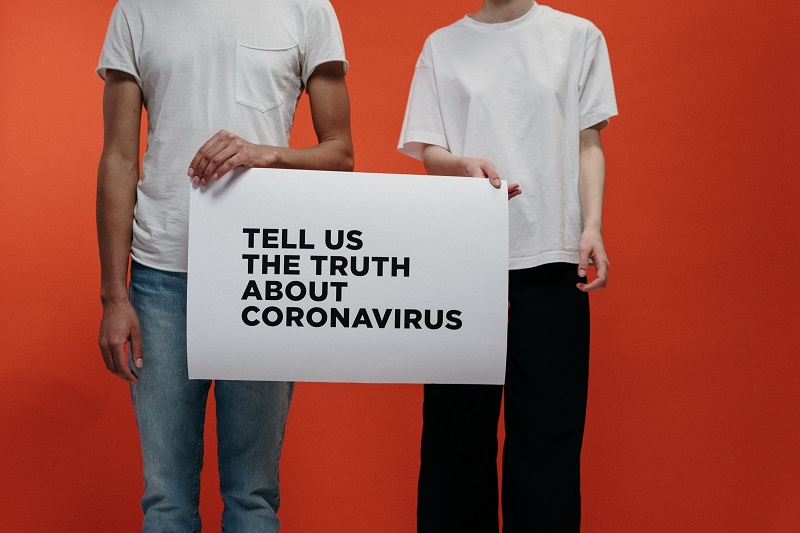 Two people holding a board seeking truth about corona virus
