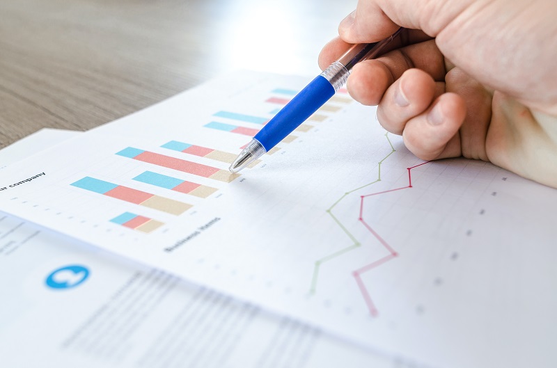 3 Exploits Of The Anchoring Effect - An image of a person pointing to statistical bar charts on a piece of paper with his or her pen (only the hand is visible in the image)