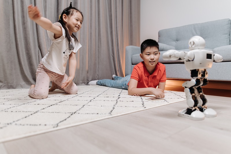 Two children playing with the same artificial intelligence robot, which looks cute in this picture instead of looking mean