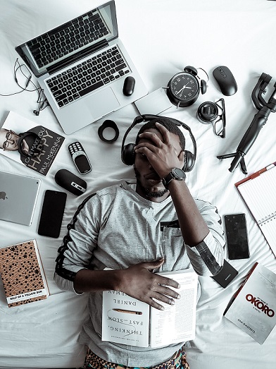 A guy lying in bed with tech devices surrounding him - a metaphor to technology dependency