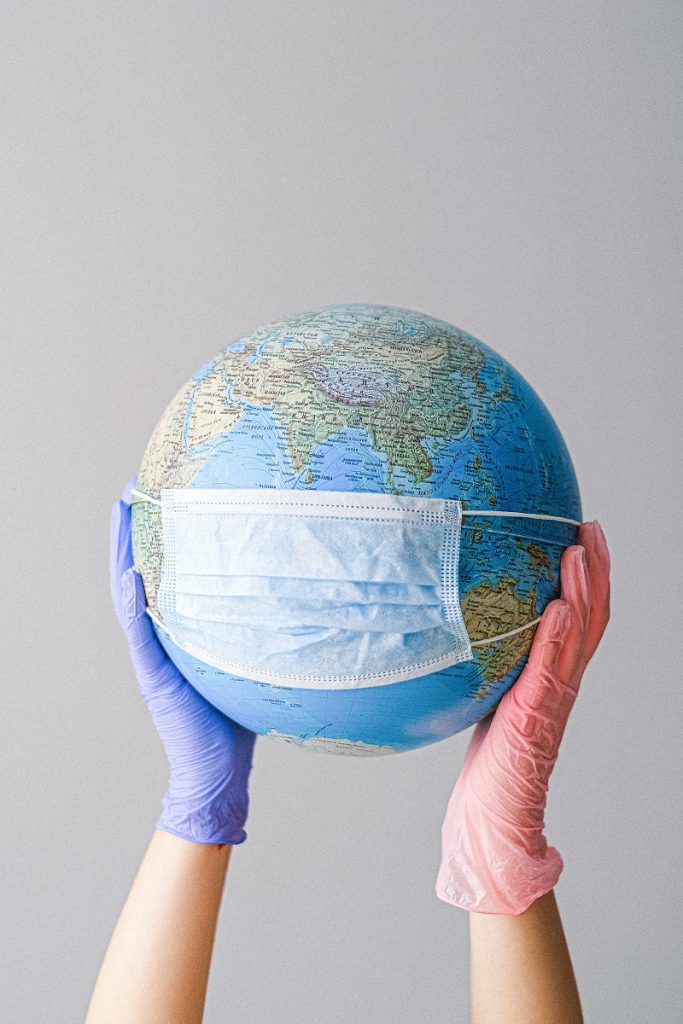 A globe that is covered by a sugical mask and held by two hands wearing surgical gloves.