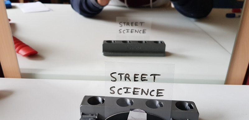 In this image, the transparent strip is not rotated around the vertical direction before it is placed in front of the mirror. In the reflection, there is no horizontal flipping. You are able to read the words "STREET SCIENCE" directly on the stirip as well as in the reflection. This proves that the mirror does not flip words horizontally.