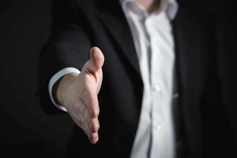 Do Startups Need Venture Capital? - A male in a dark suit offering his hand in second person mode to the viewer for shaking hands.