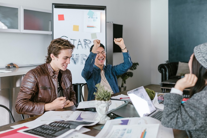 Do Startups Need Venture Capital? - A picture of three people running a startup celebrating something on a table in front of plans and a laptop.